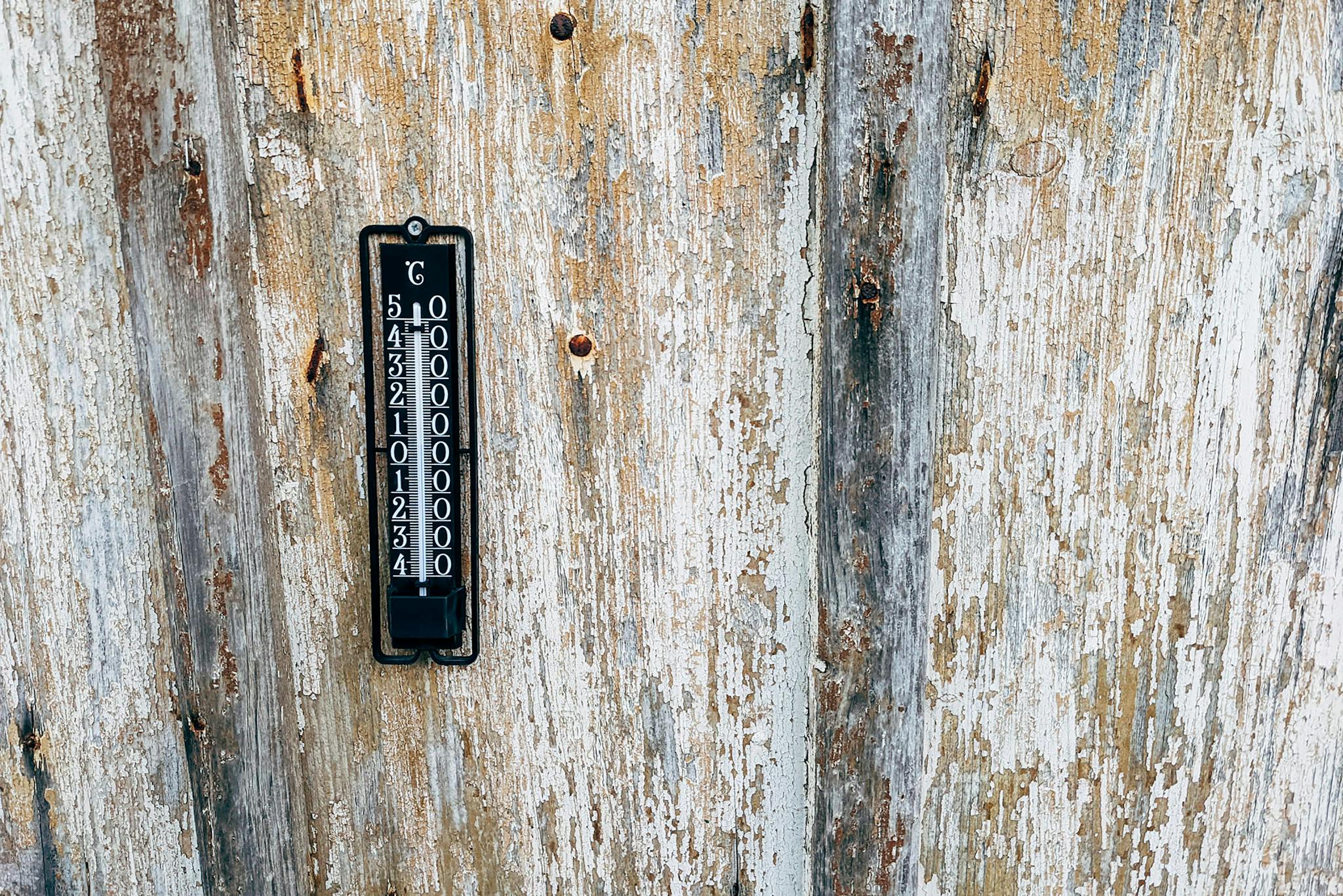 A vintage thermometer mounted on a rustic wooden wall. Perfect for themes of nostalgia and weather monitoring.