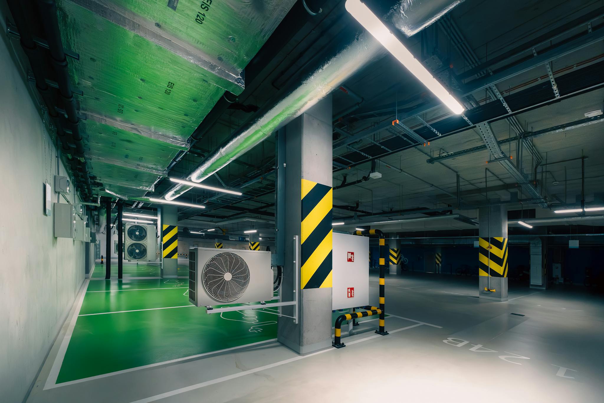 Sleek underground parking area with air conditioning units and green lighting.